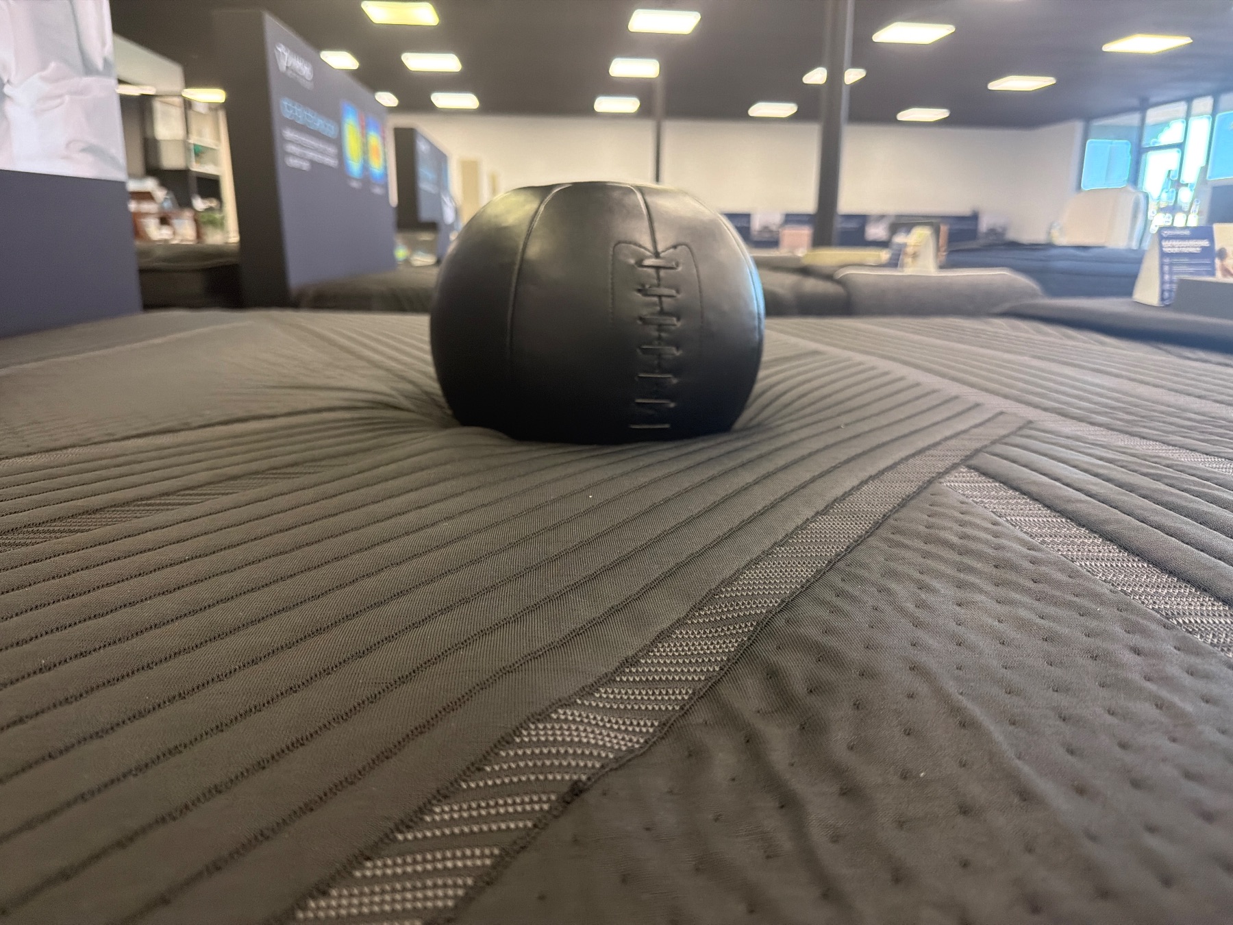 A black weighted medicine ball resting on a dark mattress cover to test surface sinkage and contouring.