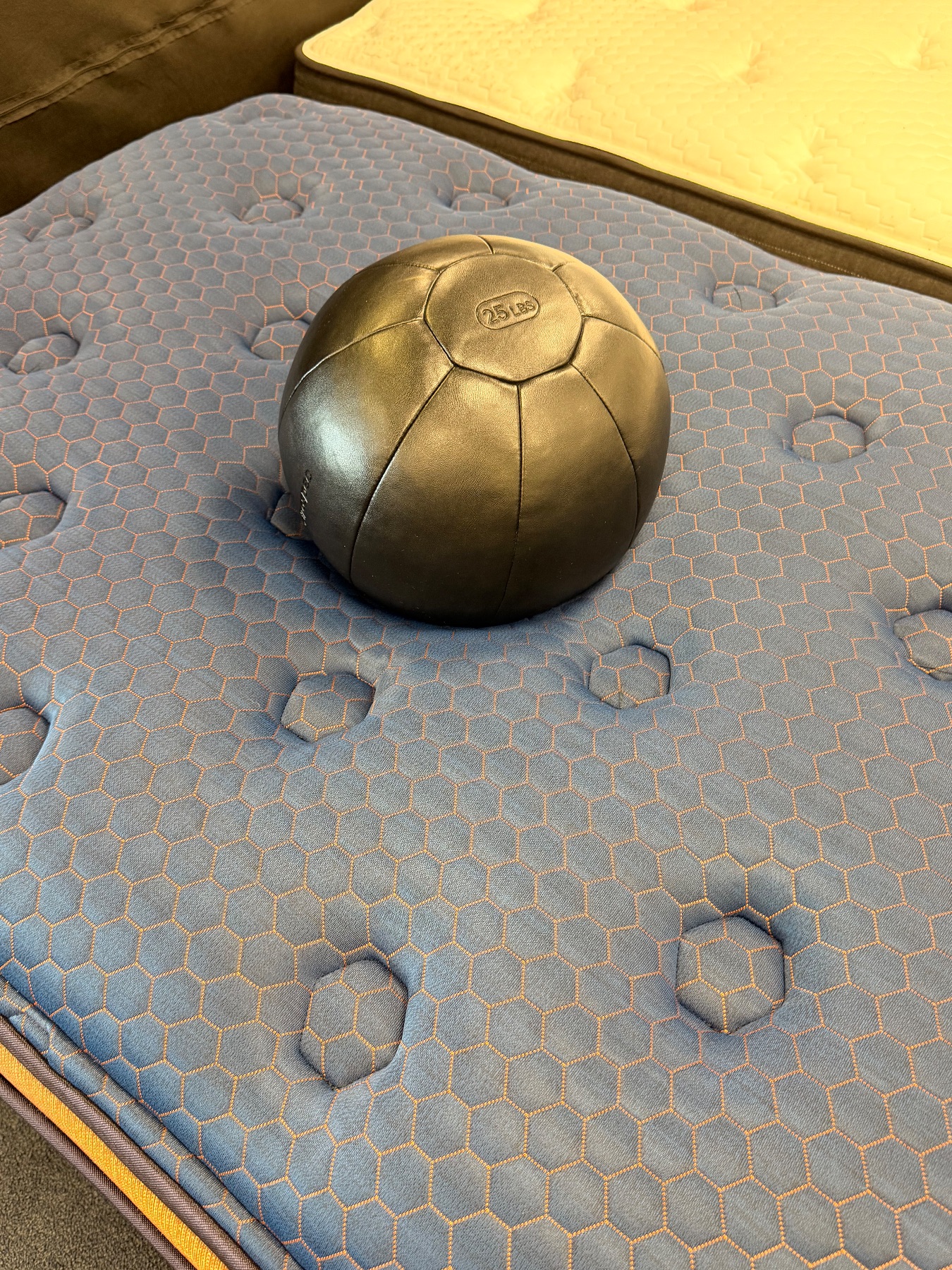 A black 25 lb weight resting on a blue honeycomb-patterned quilted mattress to test sinkage.